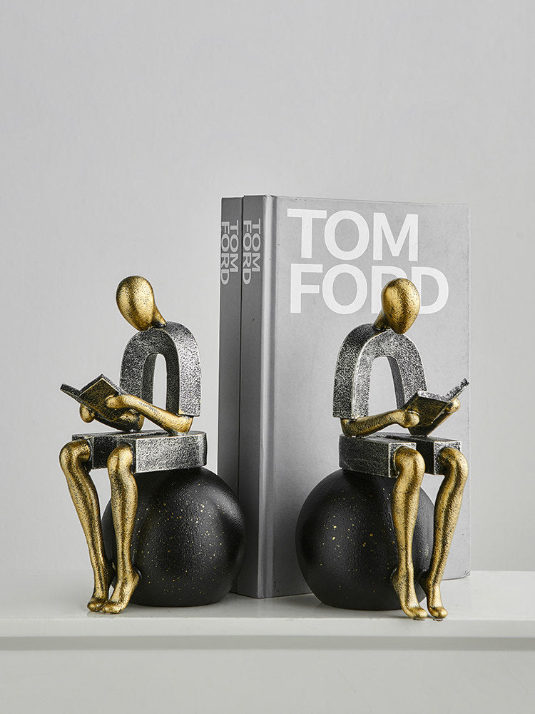 Abstract silver and gold reader figure bookends on a bookshelf.