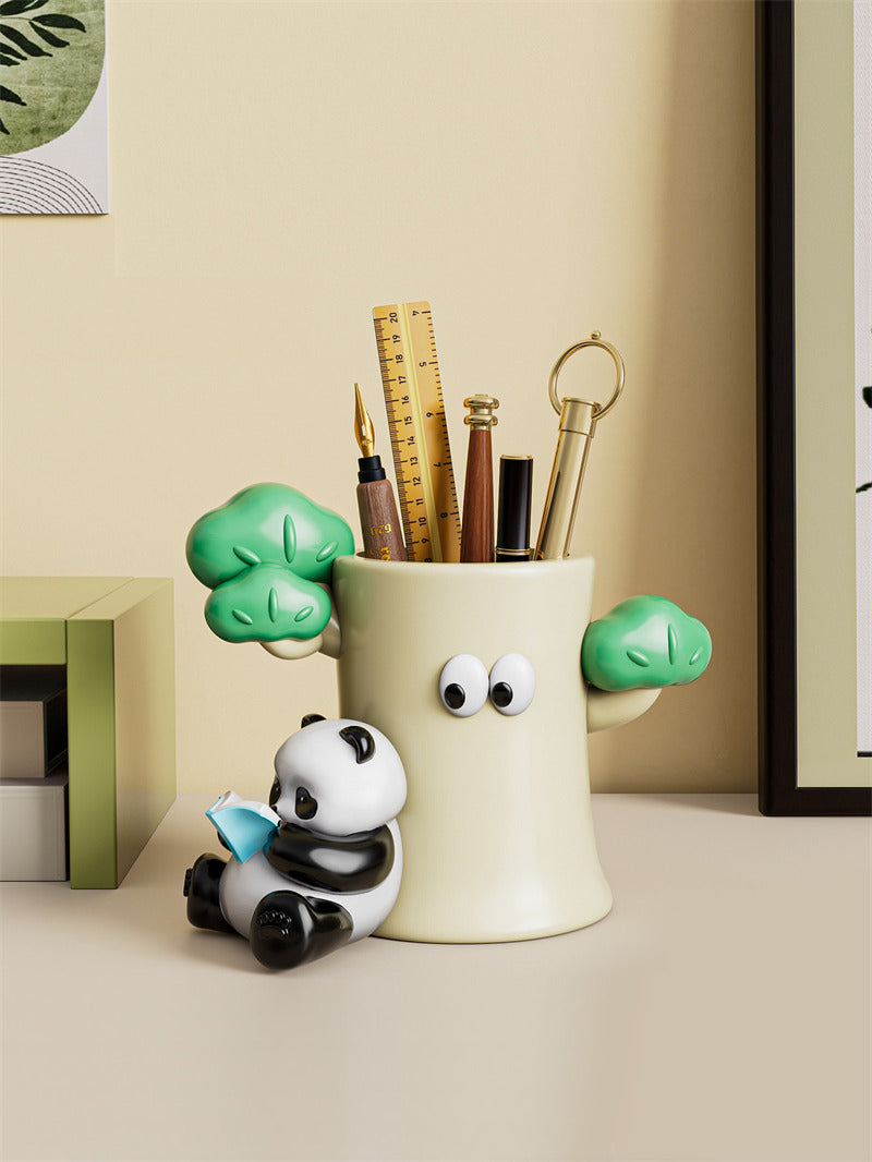Kawaii ceramic pen holder shaped like a cream tree trunk with googly eyes and a miniature 3D reading panda figurine sitting on a glossy wooden desk