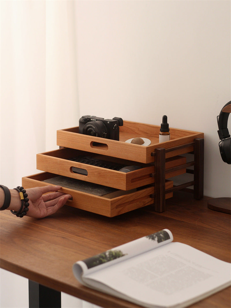 Wooden drawer unit on a desk with various items including a camera, a bottle, and a roll of paper.
